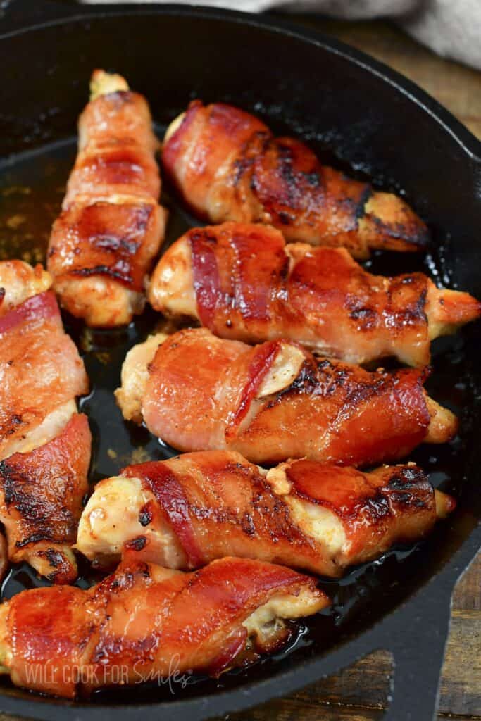 several chicken tenders wrapped in bacon cooked in the skillet.