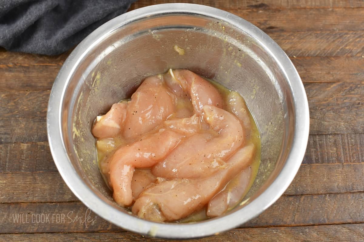 chicken tenders mixed with mustard and maple in a mixing bowl.