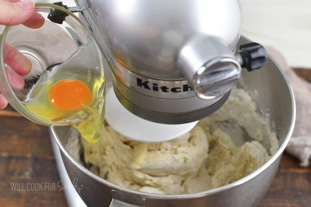 adding egg to the mixer while mixing the dough.