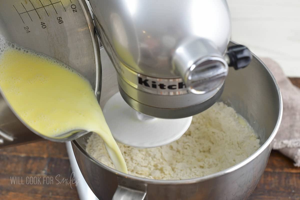 pouring in warm milk mixture while mixer is mixing the dough.