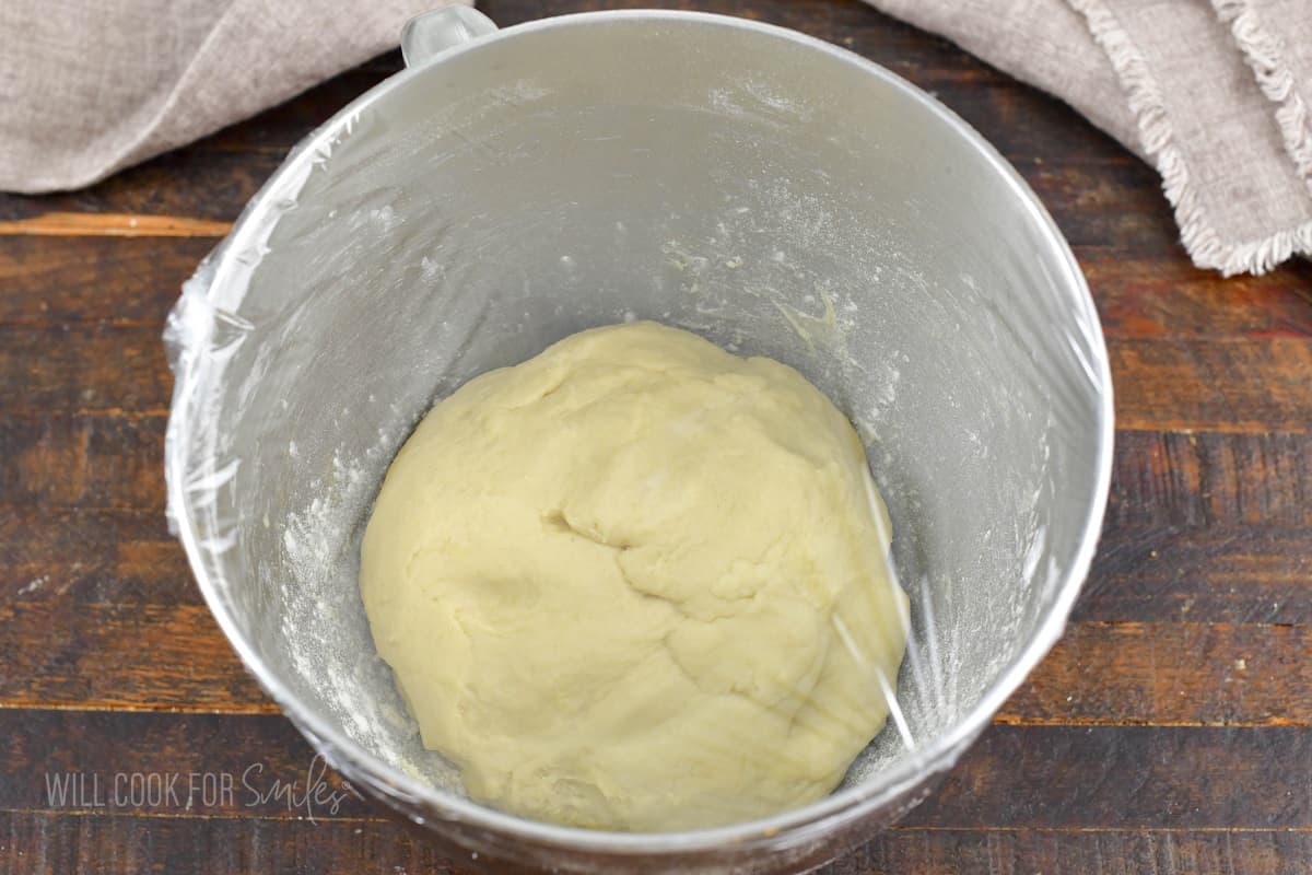 dough in the bottom of the mixing bowl covered in plastic.