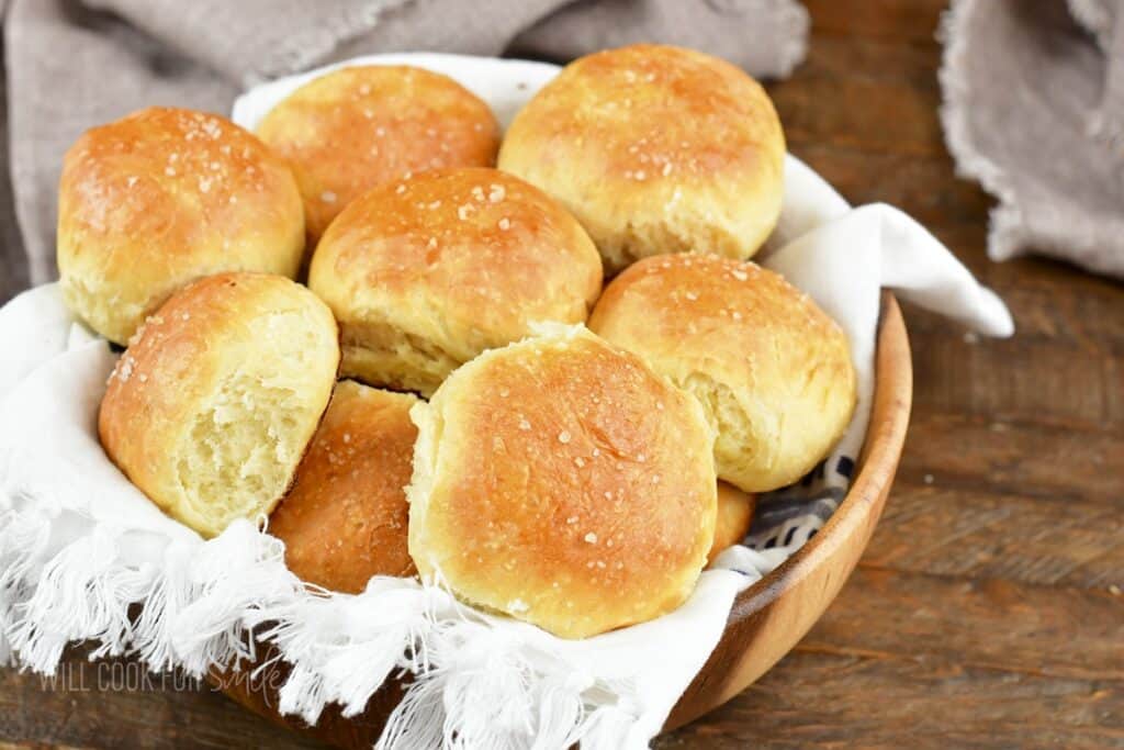 several dinner rolls in a wooden bowl with a towel.
