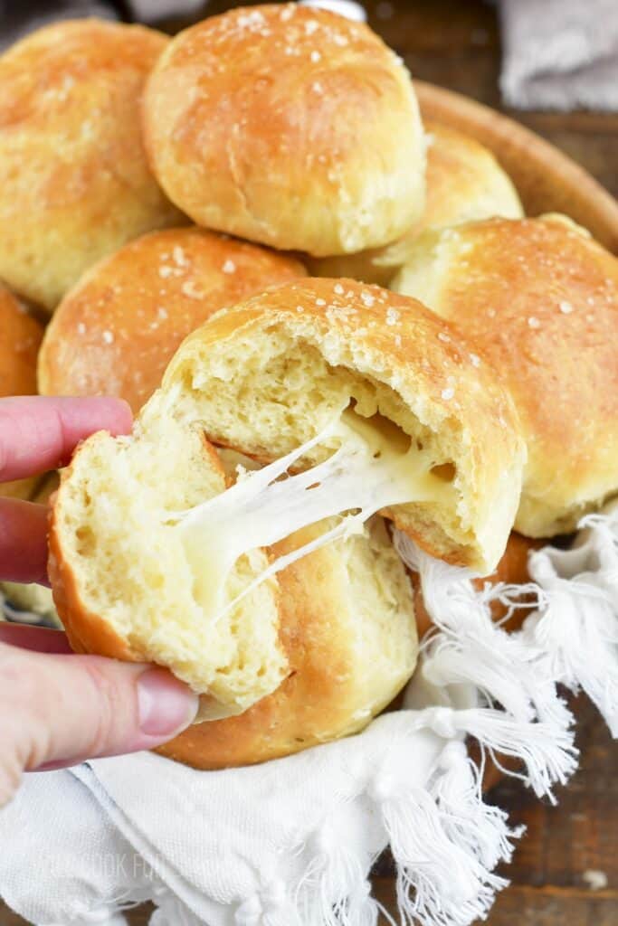 pulling part a dinner roll to show the cheesy center.