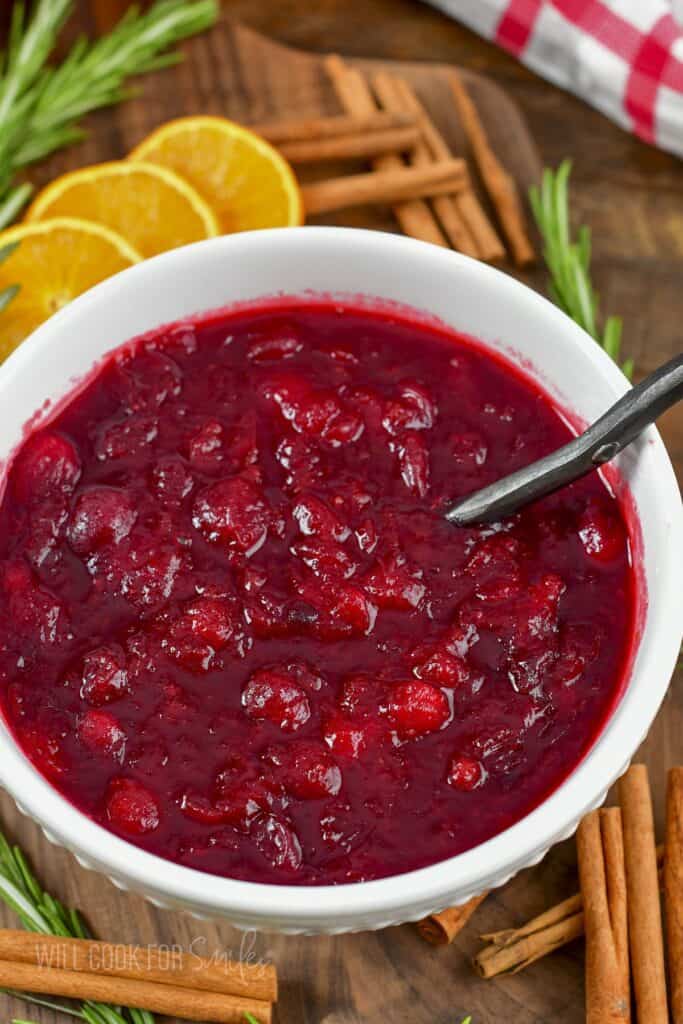 top view of cranberry sauce in a white bowl with oranges and cinnamon around.