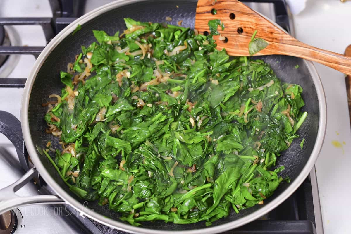 cooking spinach with onions in a large pan.