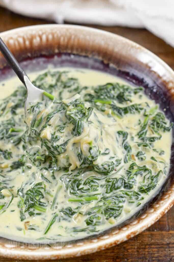 scooping out some creamed spinach from a bowl.