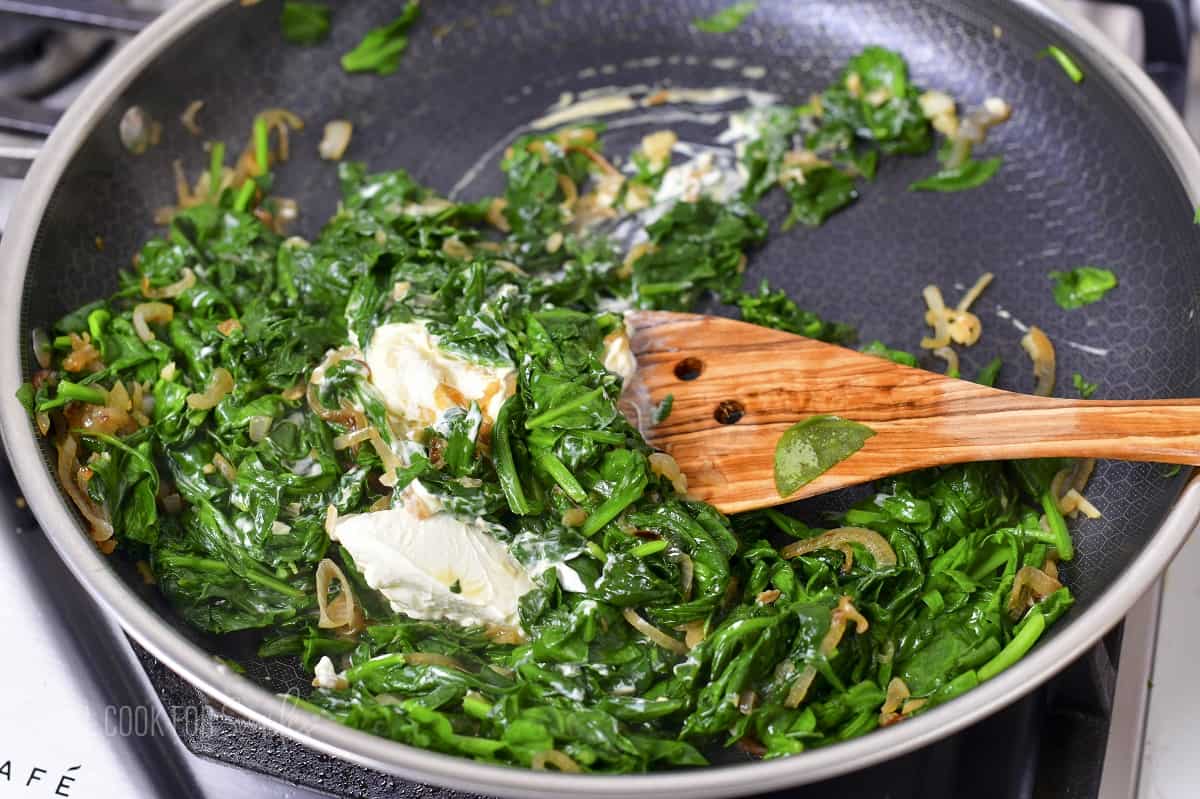 stirring in cream cheese into cooked spinach in a pan.