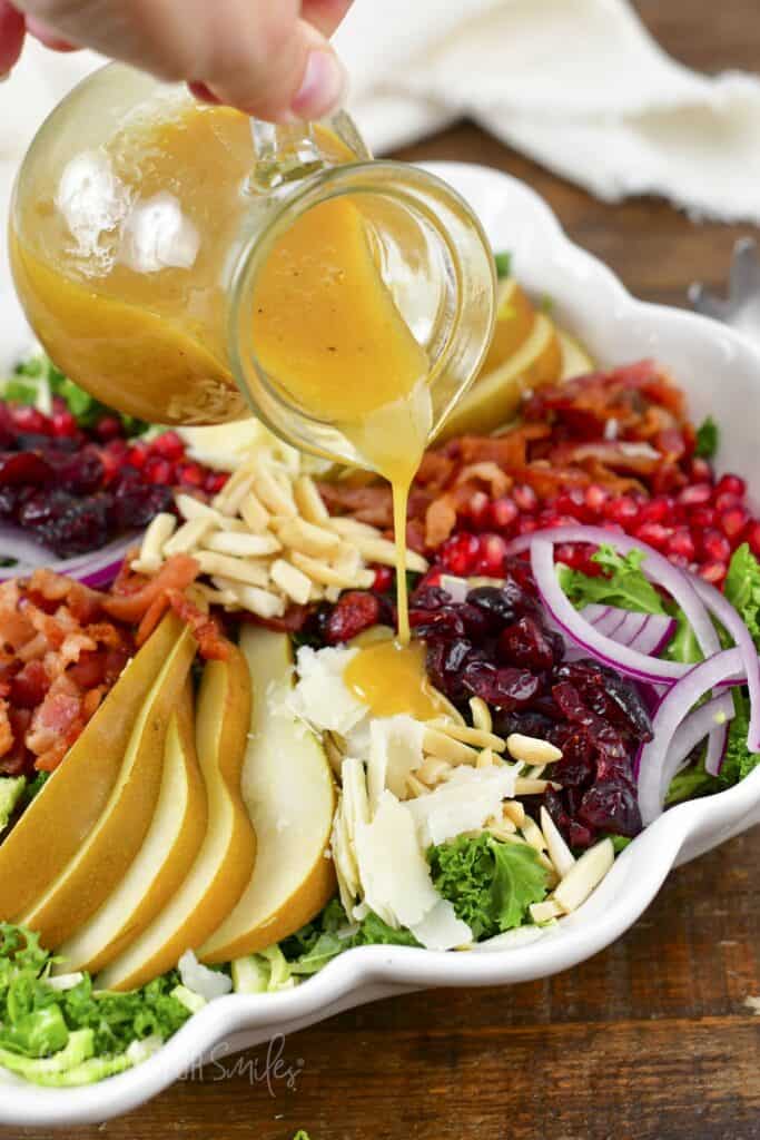 pouring mustard vinaigrette over the salad in white bowl.