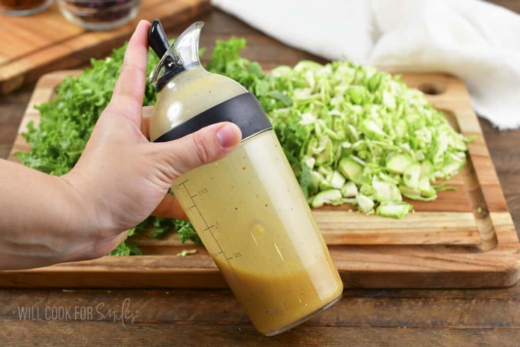 shacking mustard vinaigrette in a dressing shaker next to chopped kale.