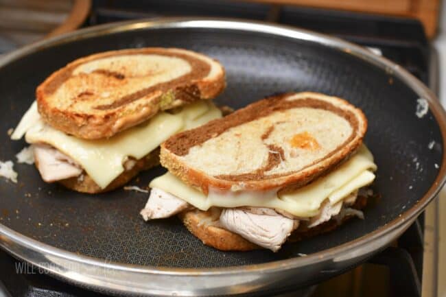 two turkey Reuben sandwiches cooking in the pan.