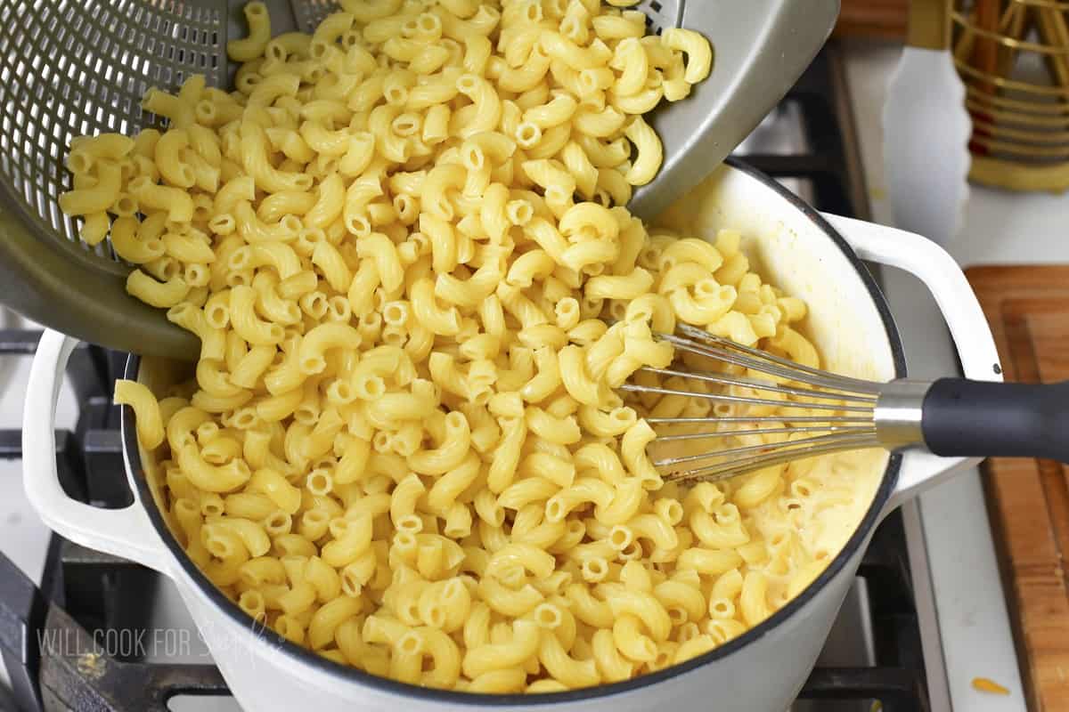 adding cooked macaroni to the pot with cheese sauce.