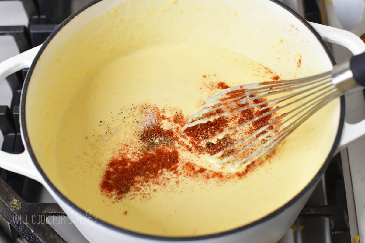 adding seasoning to the cheese sauce in a pot.