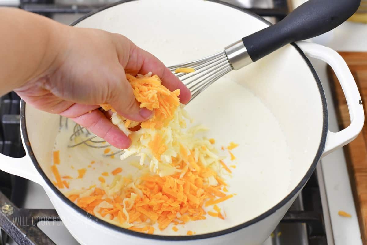 adding grated cheeses to the heated milk in a pot.