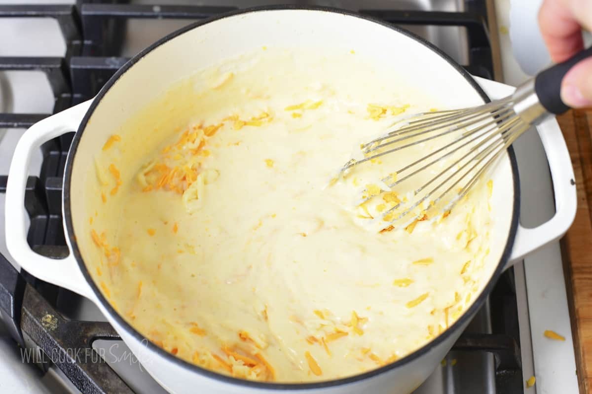 stirring together cheese sauce in a pot with a whisk.