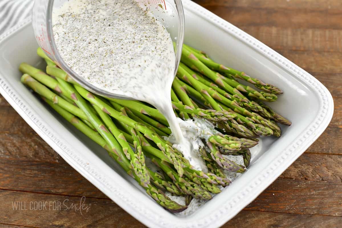 adding cream mixture to asparagus in baking dish.