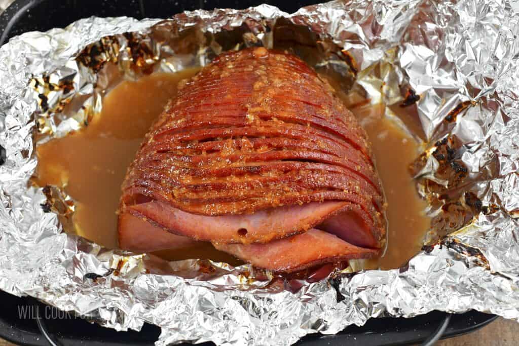 finished baked ham in foil in a roasting pan.