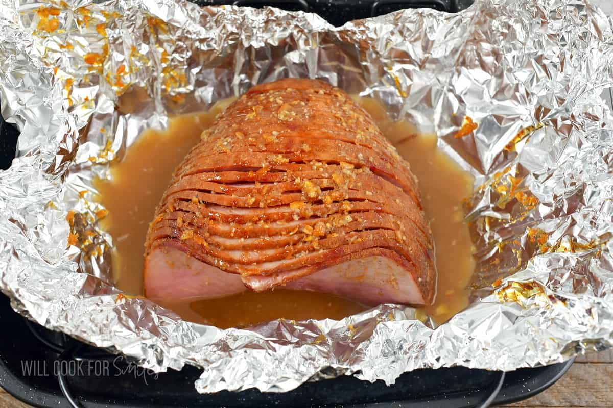 baked ham in foil in a roasting pan with foil open.