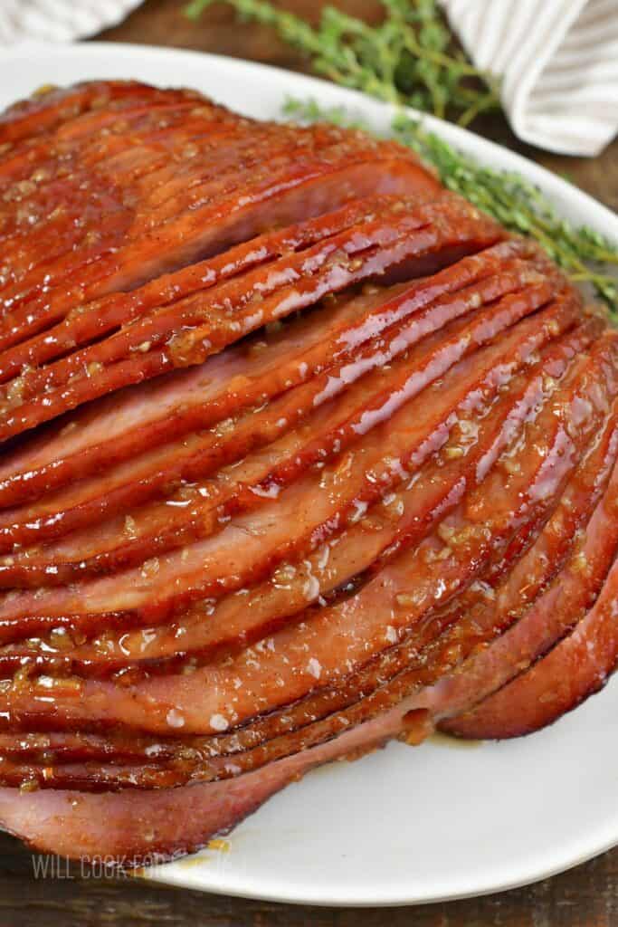 closeup of orange glazed ham on a white platter.