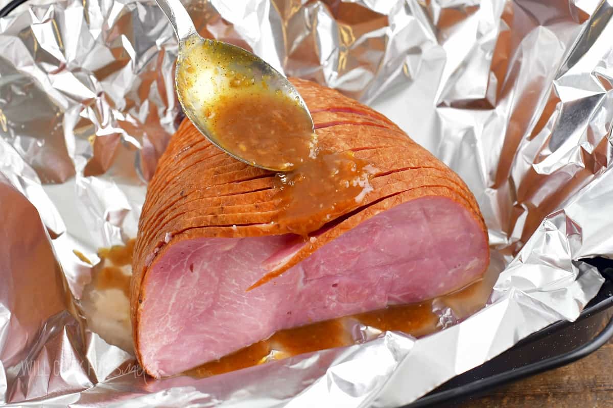 pouring orange glaze over spiral sliced ham on the foil.