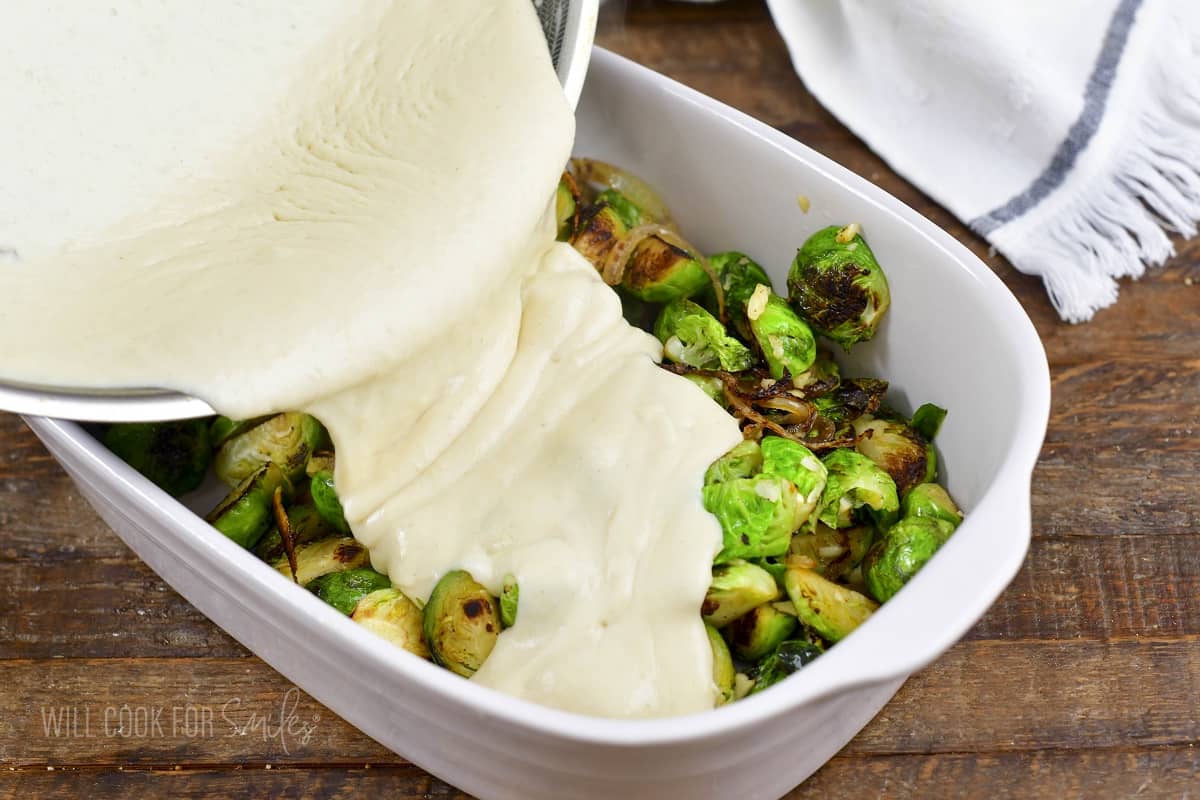 adding cream sauce to the baking dish with brussels.