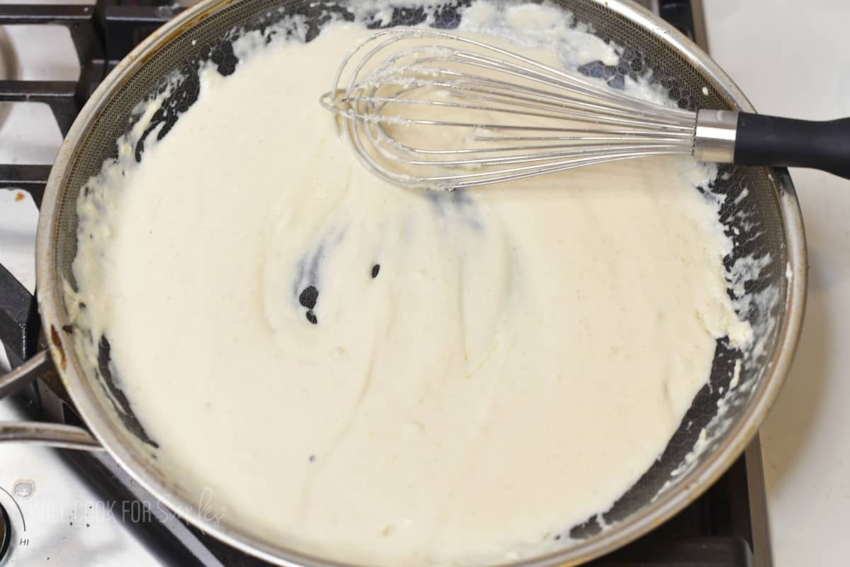 whisking creamy cheese sauce in the pan.