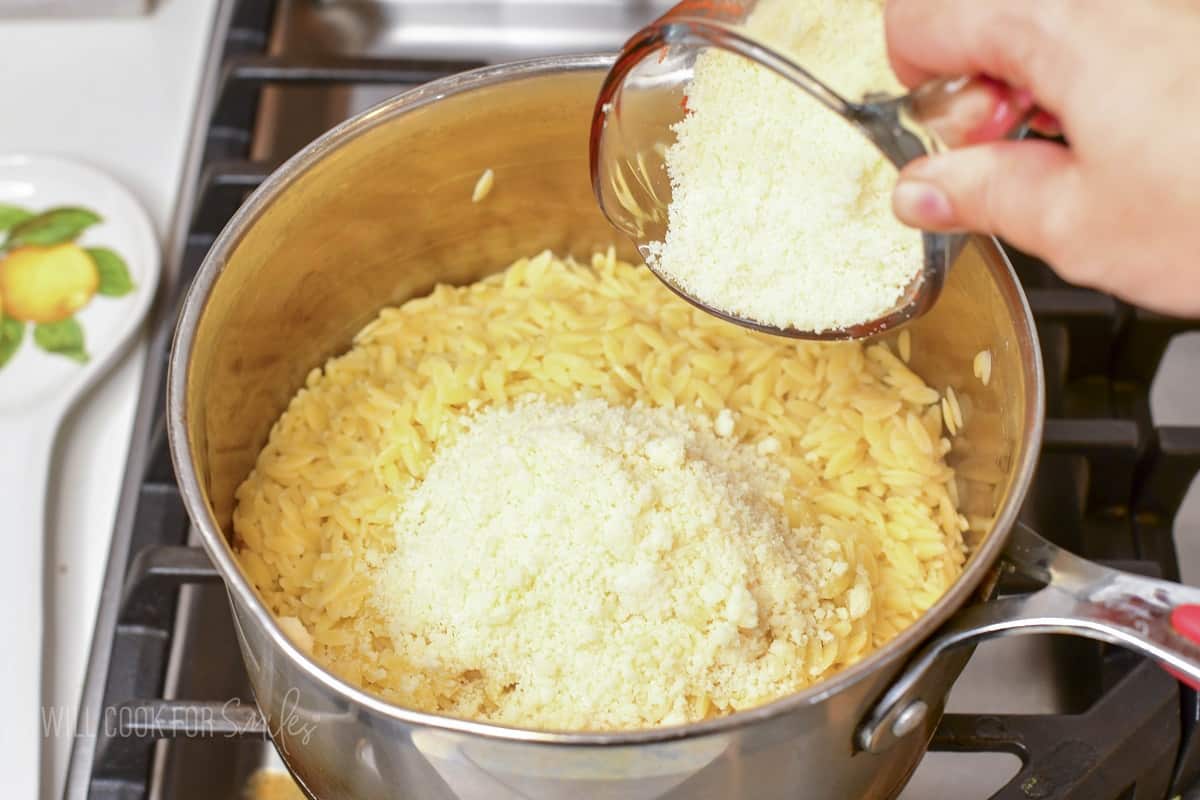 adding grated parmesan to orzo in a pot.