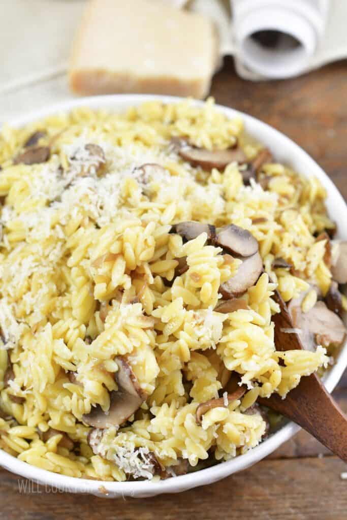 scooping out some parmesan orzo with mushrooms from a bowl.