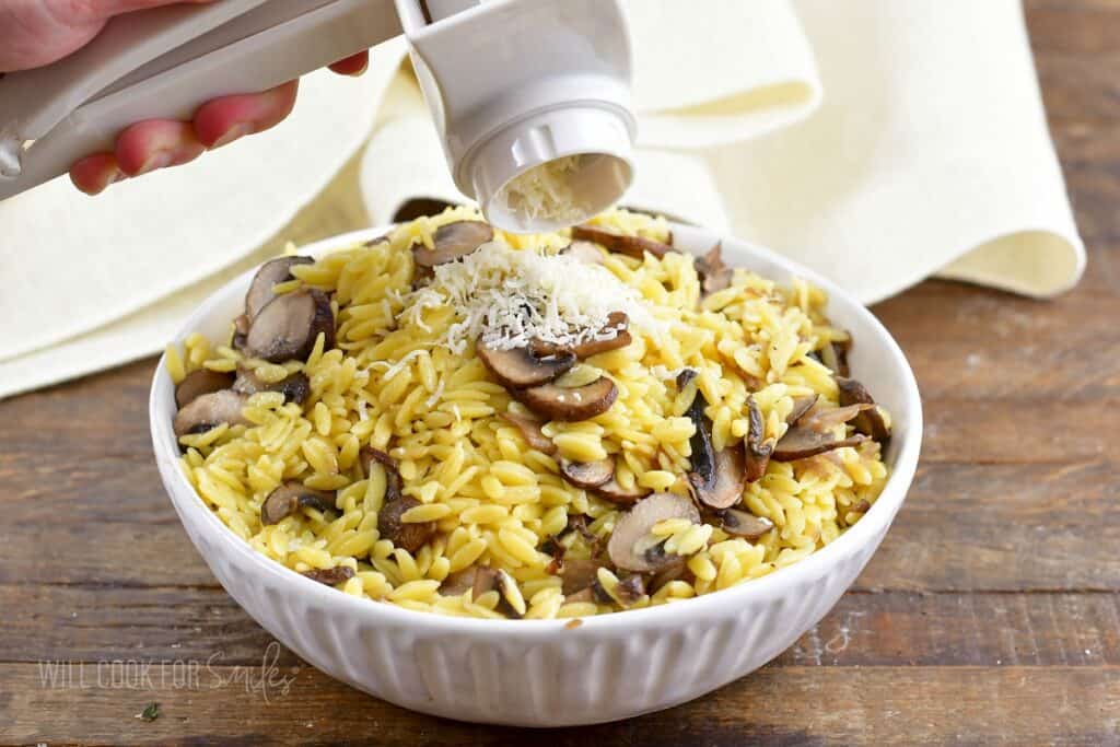 grating parmesan cheese over the bowl of orzo.