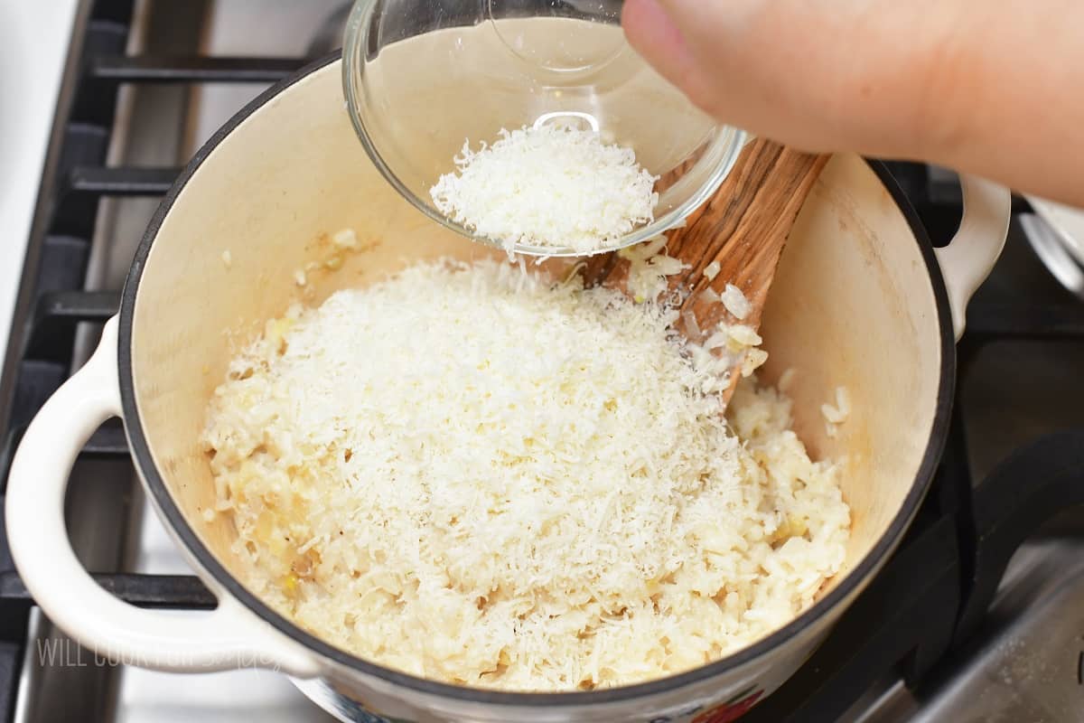 adding grated parmesan cheese to pot with cooked rice.