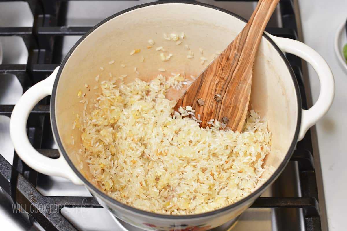 sautéing rice and onions in a white pot.
