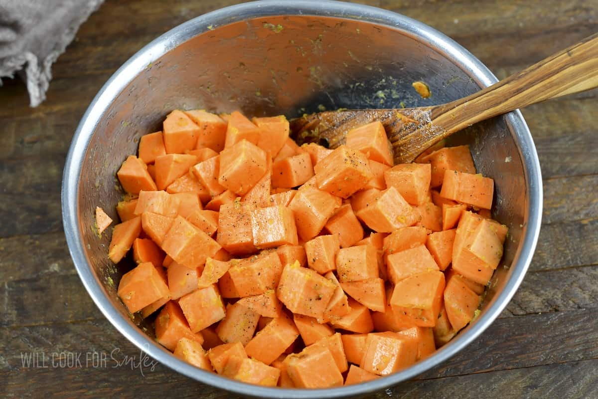 mixing cubed sweet potatoes and seasoning in a bowl.