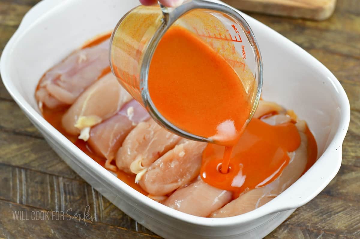 adding winger sauce to the chicken tenders in the baking dish.