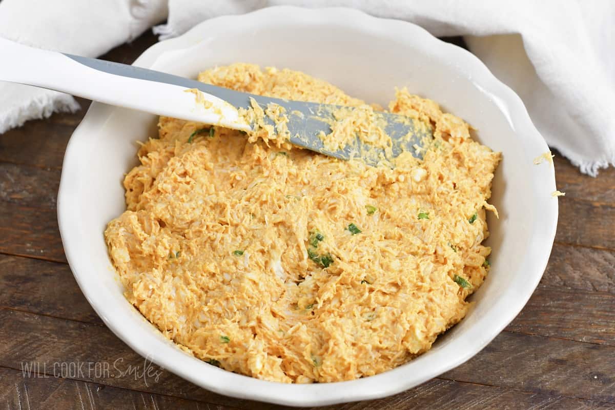 spreading mixed buffalo chicken dip in a white baking dish.