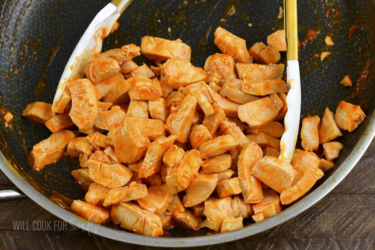 diced chicken tenders in buffalo sauce in a pan.