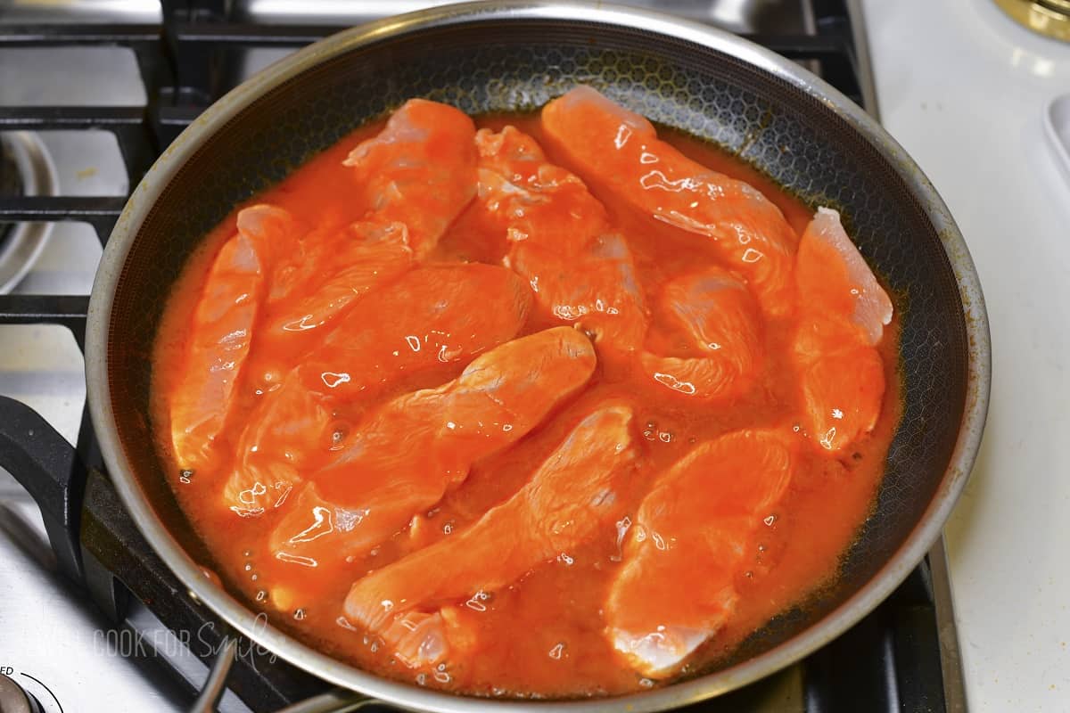 chicken tenders cooking in buffalo sauce in the pan.
