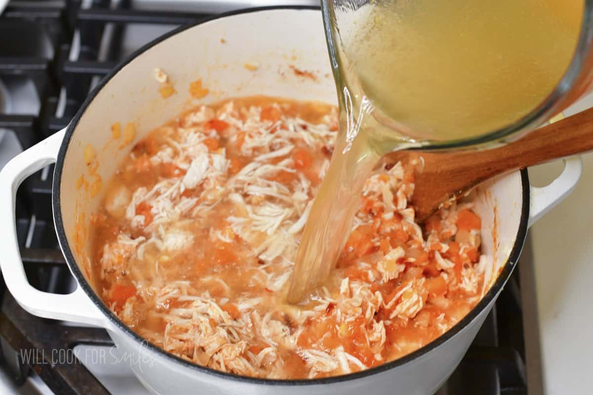 adding chicken broth to the pot with soup.