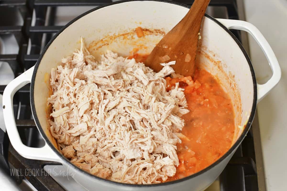 adding pulled chicken to the soup in a pot.