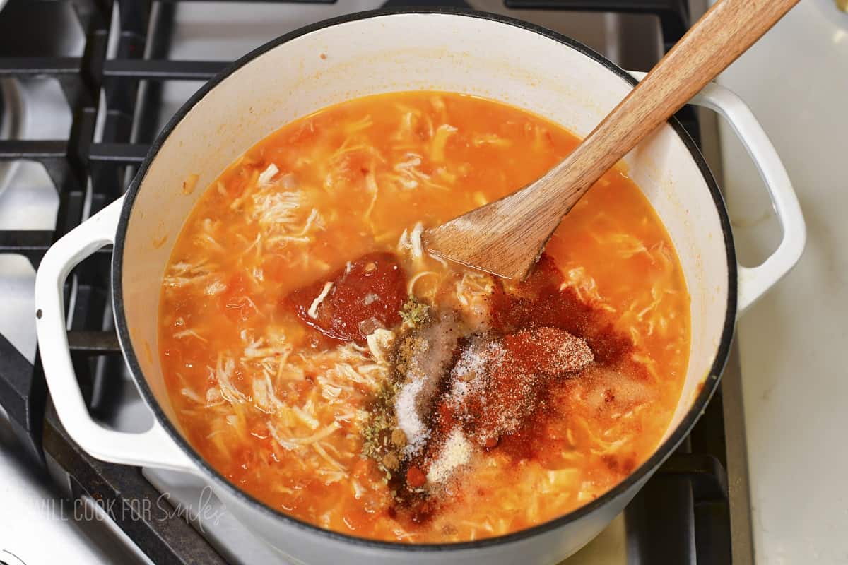adding seasoning to the soup in a pot.