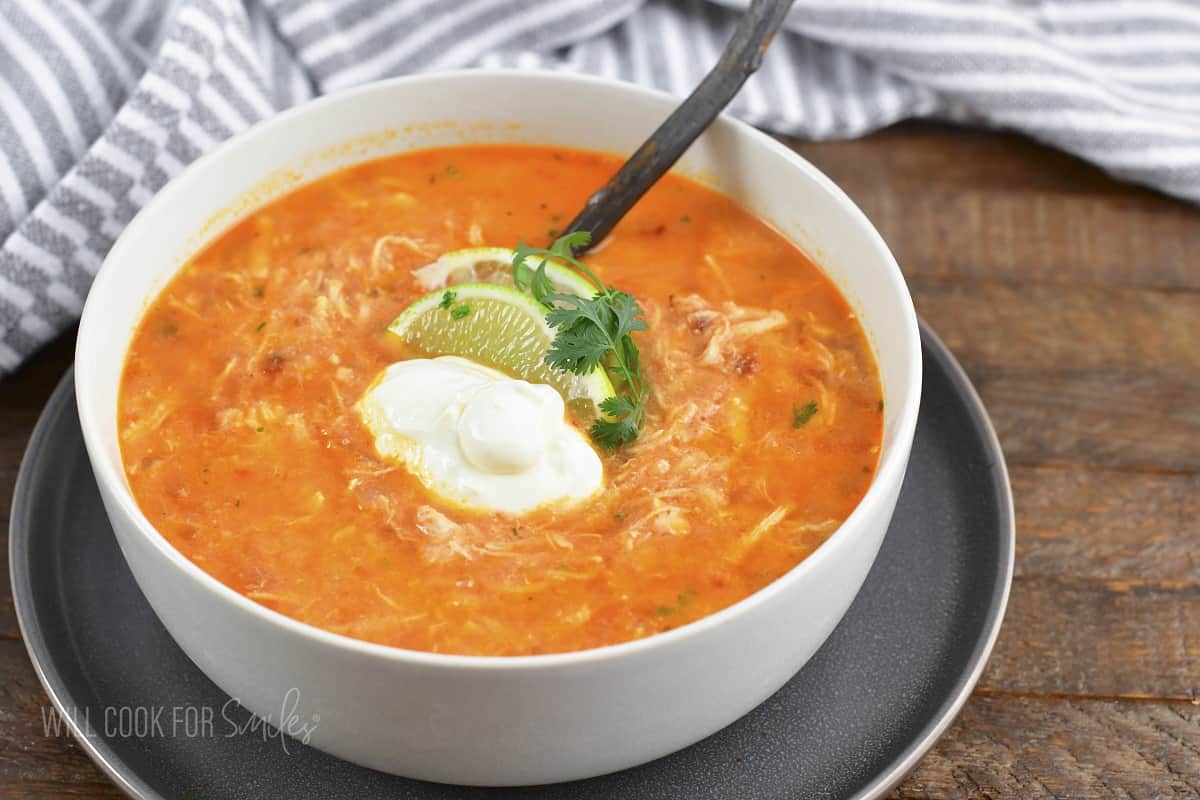 enchilada soup in a bowl inside a wide place with a spoon.