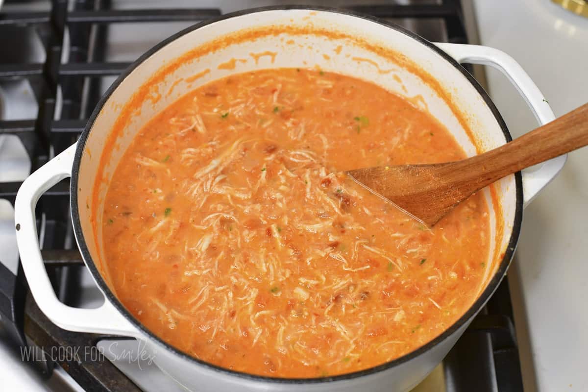 stirring the soup in a white Dutch oven with spoon.