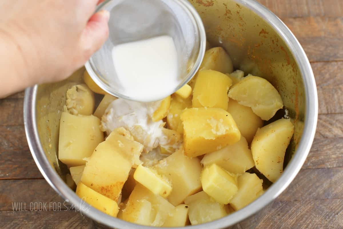 adding milk to cooked cubed potatoes in a pot.