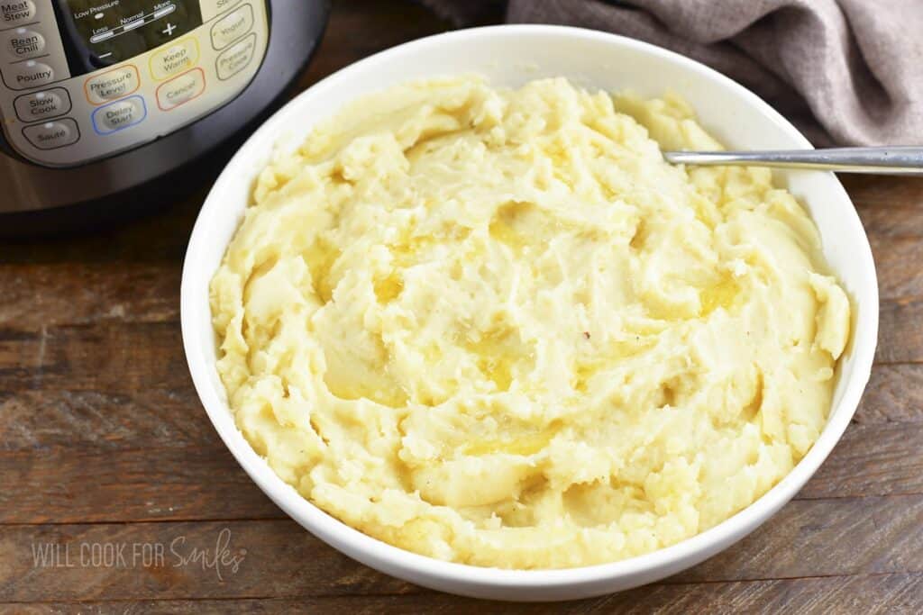closeup of mashed potatoes in a bowl topped with melted butter.