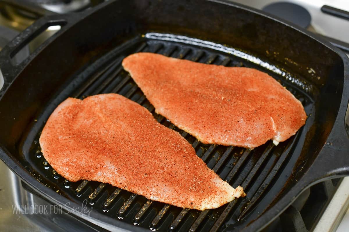 two chicken breast cutlets cooking in the skillet.