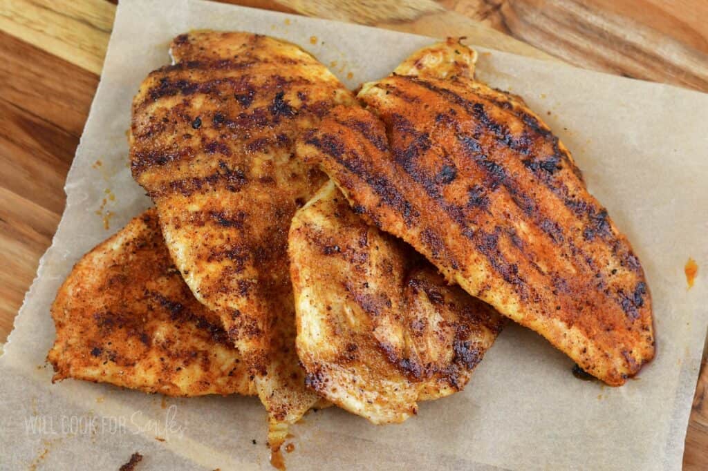 four seasoned and grilled chicken cutlets on the board.