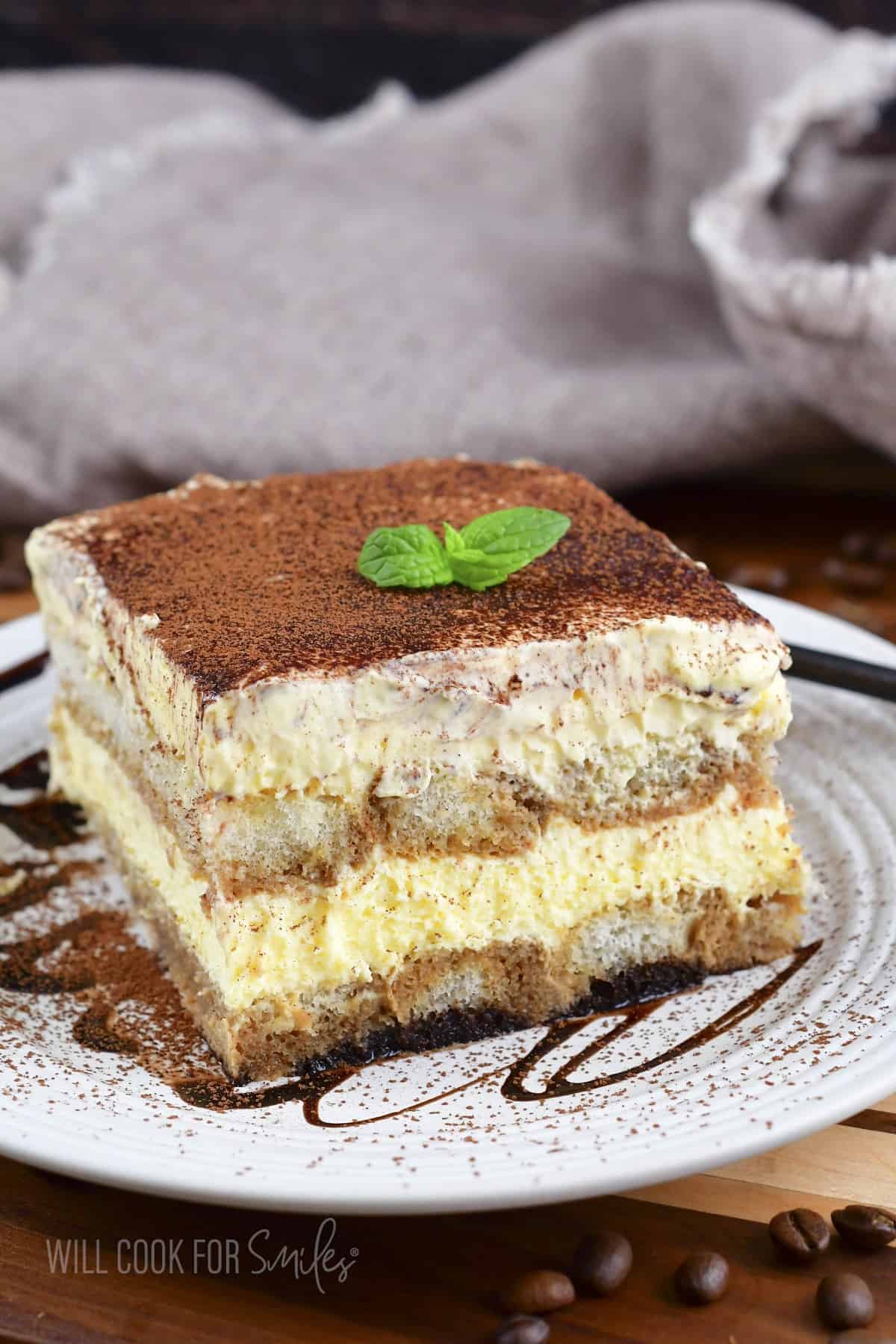 front view of a slice of tiramisu on a plate with chocolate drizze.