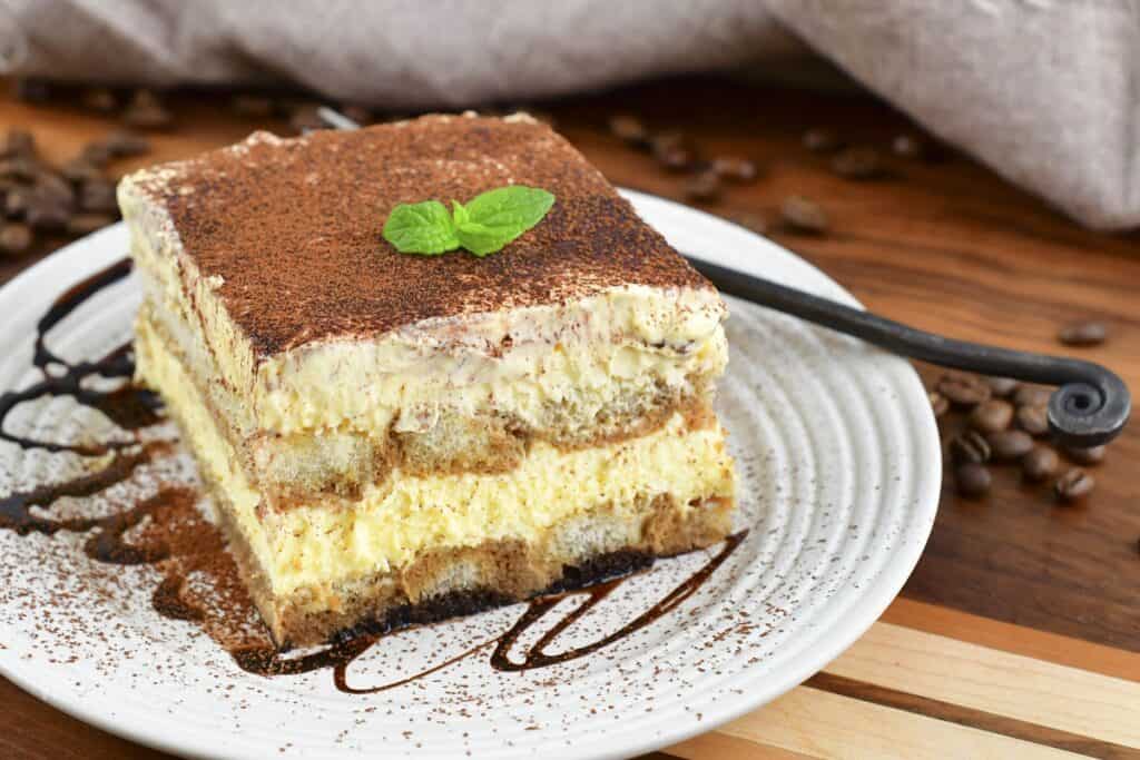 slice of tiramisu with a piece of mint on top on a plate.