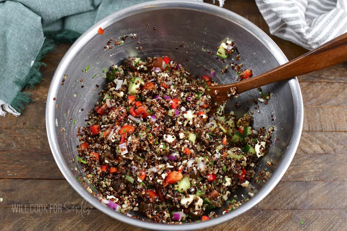 mixing quinoa salad in a metal bowl.
