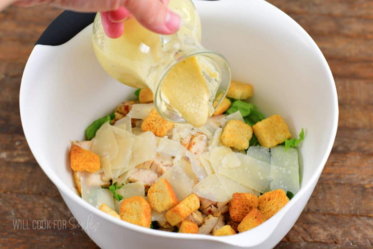 adding Caesar dressing to the mixing bowl with the salad.