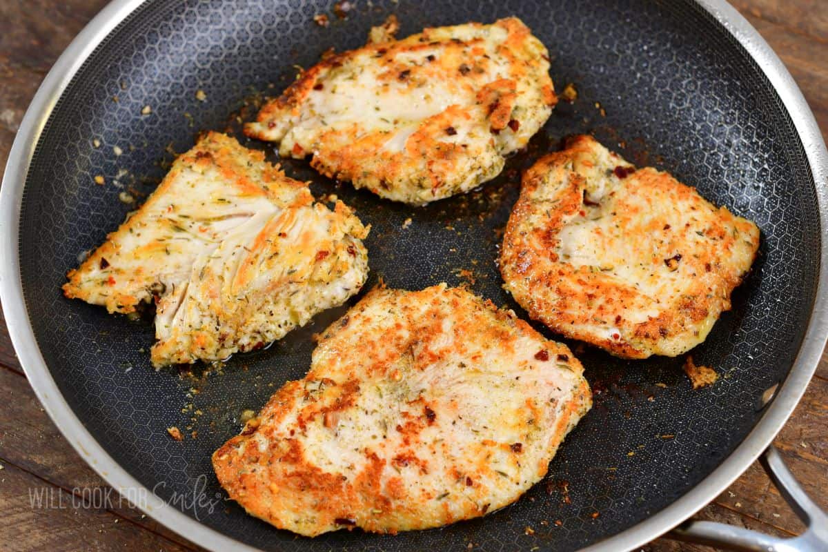 four seasoned chicken cutlets cooking in a pan.