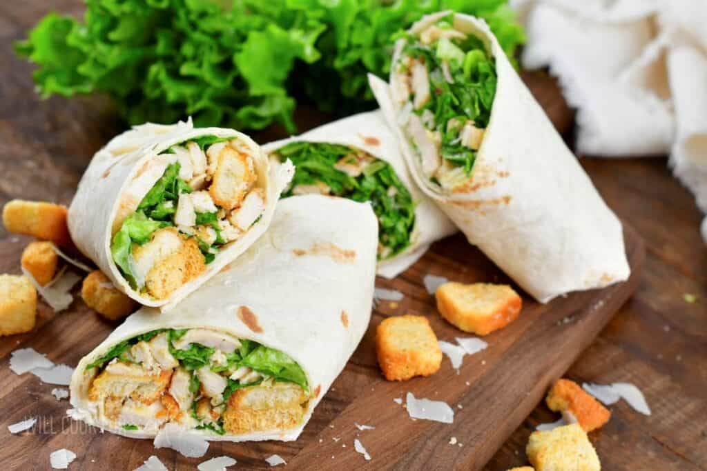 four chicken Caesar wrap halves stacked on a board.